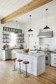 a kitchen with white walls and wooden floors, an island in the middle has three stools on it