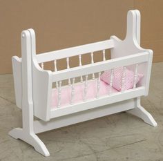 a white doll crib with pink sheets on it's sides and two pillows