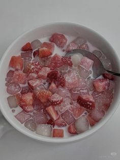 a bowl filled with ice and strawberries on top of a white table next to a spoon