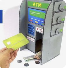 a hand holding a credit card in front of a atm machine with money coming out of it