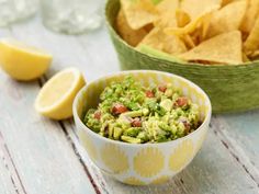 a bowl filled with guacamole and chips next to a basket of tortilla chips