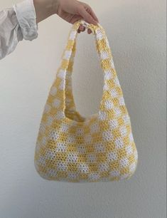 a hand holding a yellow and white crocheted bag on a hook against a wall