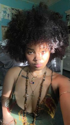 a woman with an afro is posing for the camera in her bedroom, wearing necklaces