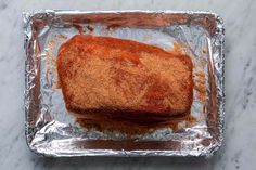 a square piece of meat covered in seasoning on top of aluminum foil