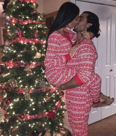 a man and woman kissing in front of a christmas tree