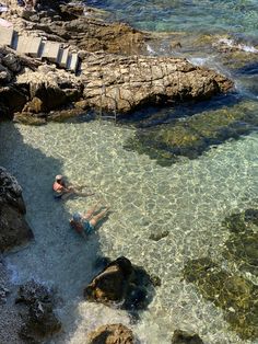 two people are swimming in clear water near the rocks and beach area with steps leading up to them