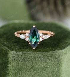 an emerald colored ring with white and pink diamonds sits on top of a green velvet