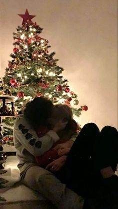 two people sitting in front of a christmas tree