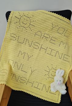 a yellow crocheted blanket with a white stuffed rabbit on the chair next to it