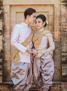 a man and woman standing next to each other in front of a brick wall wearing traditional thai garb