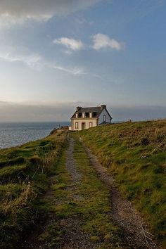 a house sitting on top of a lush green hillside next to the ocean with a blue sky