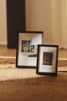 two black and white frames sitting on top of a wooden table next to each other