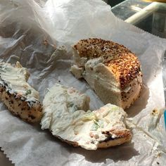 there is a bagel with cream cheese and other items on the paper wrapper