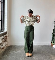 a woman standing in front of a window with her hands on her hips and arms behind her back