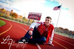 a young man sitting on the side of a track with an american flag in the background