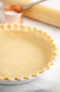 an uncooked pie crust sits on a counter next to baking utensils