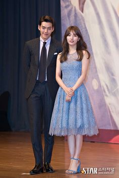 a man and woman standing next to each other in front of a stage with a poster behind them