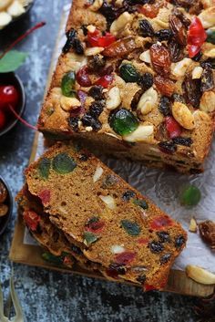 two slices of fruit and nut bread sitting on top of a cutting board next to bowls of cherries