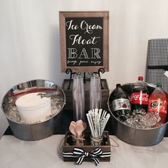 a table topped with two metal pans filled with ice cream and drinks next to a chalkboard sign