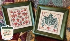 two framed cross - stitch pictures sitting next to each other on top of a quilt