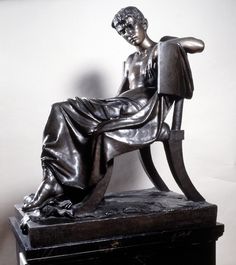 a bronze statue sitting on top of a black table next to a white wall and floor