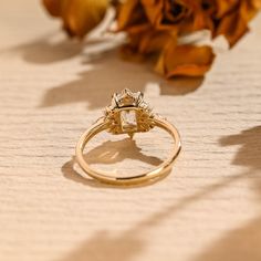 a close up of a diamond ring on a table with flowers in the back ground