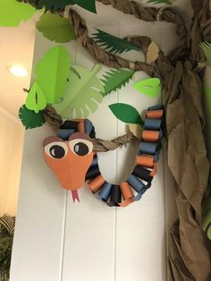 an animal made out of paper and some leaves on the wall next to a plant