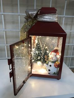 a lighted lantern with a snowman and christmas tree in the front, sitting on a table