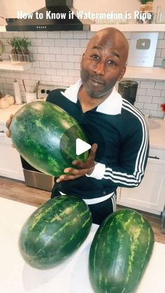 a man sitting on top of a kitchen counter holding a large watermelon in his hands