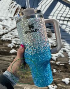 a person holding up a blue and silver glittered tumbler cup in the snow