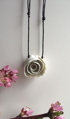 three necklaces hanging on a wall with flowers in the foreground and one being made out of paper