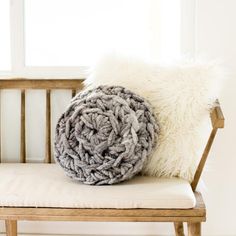 a gray and white blanket sitting on top of a wooden bench next to a pillow