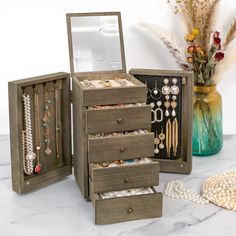 an assortment of jewelry sits on a marble counter top next to a vase with dried flowers