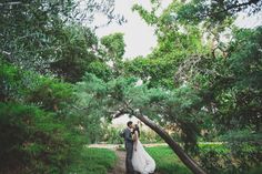 a bride and groom standing under a tree in the middle of a path surrounded by greenery