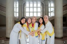 a group of young women standing next to each other in front of large columns and windows