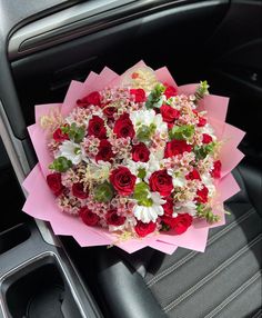 a bouquet of red and white flowers sitting on top of a pink paper in a car