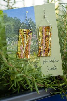 Inspired by summer walks through wildflower meadows, these Meadow Walk earrings are handcrafted with yarn, string, beads, and other mixed media on a fabric base. Each earring is unique. You will receive a complimentary pair from the same meadow, but each earring will have a separate view.  Scrappy Trails Art is all about upcycling and stashbusting textile scraps into wearable art. The yarn used in Meadow Walk constructed a gorgeous goldenrod lace poncho and a perfect lazy winter morning cabled r Mixed Media Earrings, Textile Scraps, Summer Walks, Lace Poncho, Winter Morning, Winter Mornings, Wearable Art, Wild Flowers, Jewelry Earrings Dangle