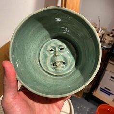 a hand holding a green bowl with a face on it's front and bottom