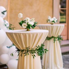 two tables with white flowers and greenery on them