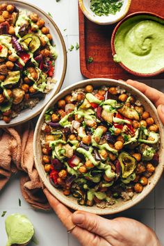 two hands holding a bowl filled with salad next to bowls of guacamole