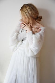 a woman in a white dress with her hands on her chest, leaning against a wall