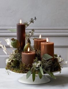 candles are arranged in a bowl with moss and leaves on the table next to each other