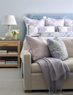 a couch with pillows and blankets on it next to a night stand filled with books