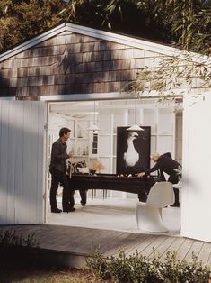 two men are playing pool in the back of a white shed with an open door