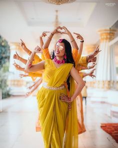 woman in yellow sari dancing with her hands up to the ceiling and other dancers behind her