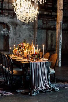 a dining room table with candles and flowers on it, in front of a chandelier