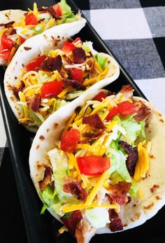 three tortillas with bacon, lettuce and tomatoes on a black tray