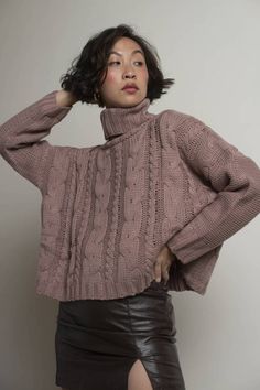 a woman wearing a brown sweater and black leather skirt is posing for the camera with her hands on her head