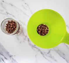 a green measuring cup filled with dog food on top of a white marble countertop