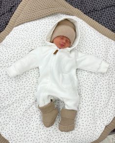 a baby is laying down on a blanket and wearing a white outfit with brown trims